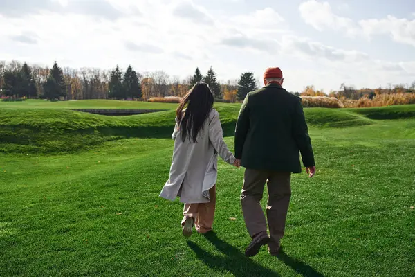 A loving couple dressed in cozy autumn attire strolls together across a lush green meadow. — Stock Photo