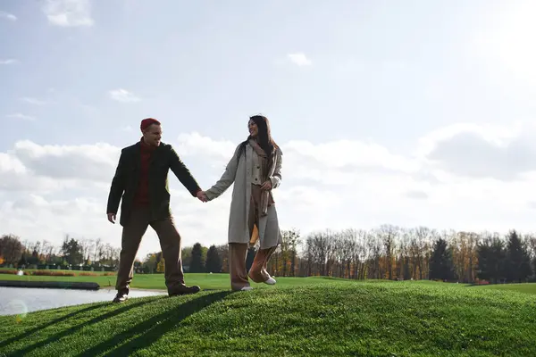 A couple in cozy autumn attire walks hand in hand, basking in the warmth of the sunlit day. — Stock Photo