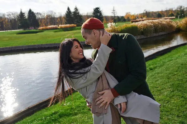 A couple enjoys a tender moment outdoors, wrapped in cozy attire amidst autumn scenery. — Stock Photo