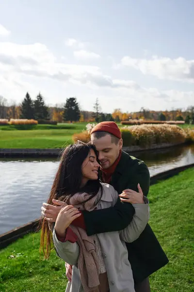 A loving couple enjoys a tender moment, wrapped in autumn attire, near a peaceful lake. — Stock Photo