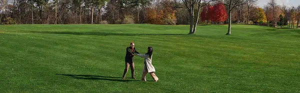 Un couple aimant tourne ensemble sur une pelouse verte vibrante, entourée de feuilles d'automne et de chaleur. — Photo de stock