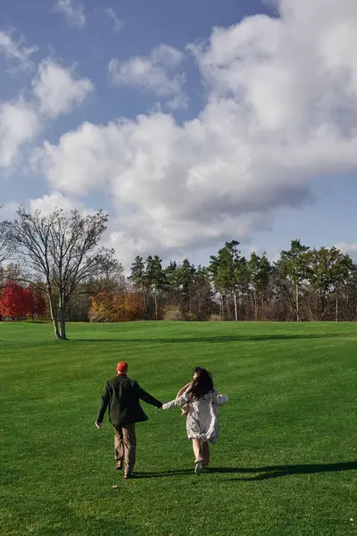 A couple in cozy clothes strolls hand in hand through a colorful autumn landscape. — Stock Photo