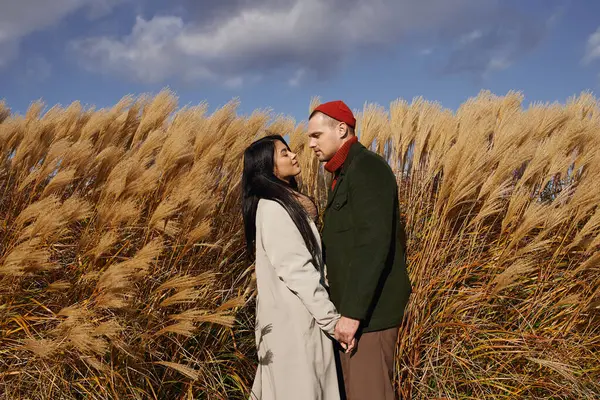A loving couple stands close, wearing warm autumn outfits, surrounded by tall golden grasses. — Stock Photo