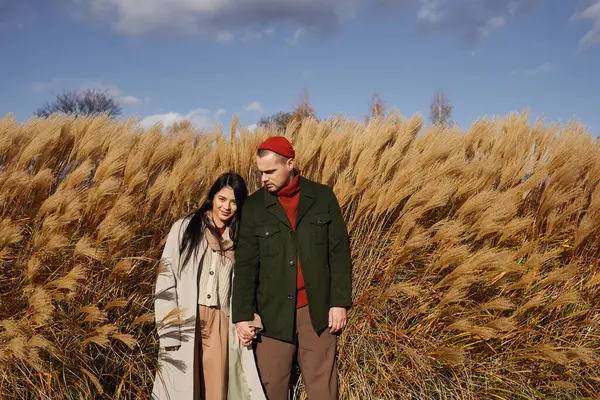 Wrapped in warmth and affection, a couple enjoys their autumn stroll through tall golden grasses. — Stock Photo