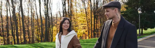 A couple dressed in warm autumn clothing walks hand in hand through vibrant fall landscapes. — Stock Photo