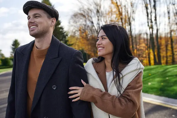 A couple walks hand in hand through a park, embracing the warmth of autumn in their outfits. — Stock Photo