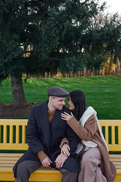 A couple enjoys each others company on a yellow bench amid autumn colors. — Stock Photo