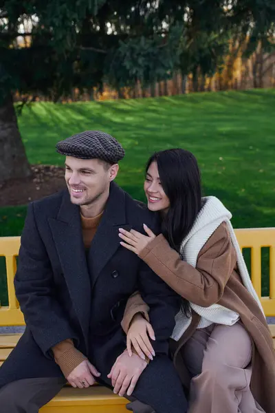 A couple smiles lovingly while cuddling on a yellow bench, surrounded by autumns vibrant colors. — Foto stock