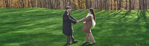 A couple in warm, stylish autumn outfits holds hands amidst a vibrant, leaf strewn landscape. — Stock Photo