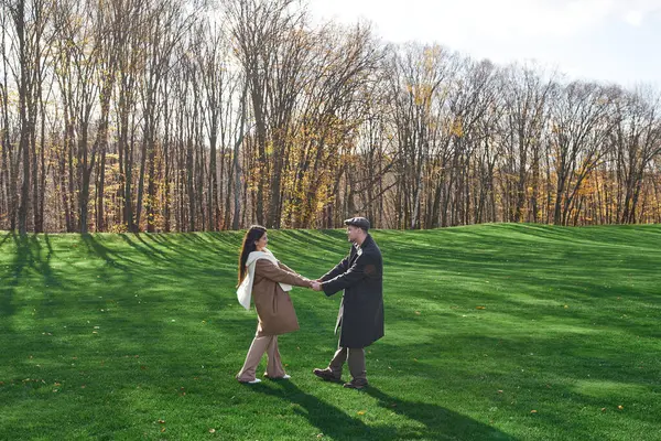 A couple dressed in cozy autumn attire enjoys each other company on a sunny day in a park. — Stock Photo