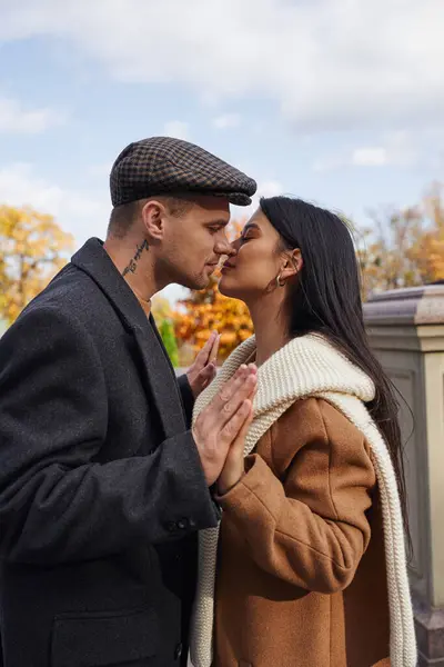 A couple shares a tender kiss, embracing the warmth of autumn in a beautiful outdoor space. — Stock Photo