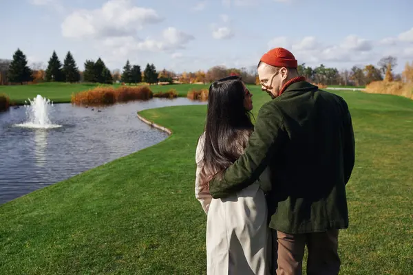 A couple enjoys a warm autumn day, wrapped in each others embrace near a tranquil lake. — Stock Photo