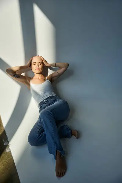 A young woman with alopecia rests elegantly on the floor, basking in soft light. — Stock Photo