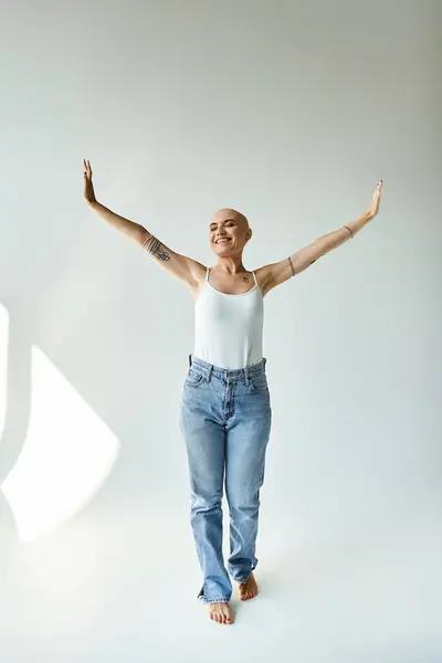 A joyful young woman expresses confidence, showcasing her baldness and tattoos in a calm space. — Stock Photo