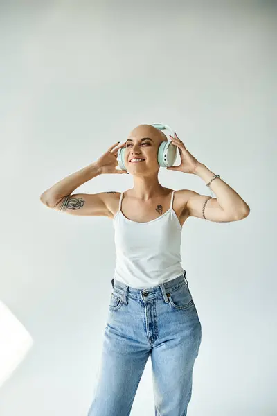 A young bald woman with alopecia dances joyfully, wearing large headphones in a stylish studio. — Stock Photo