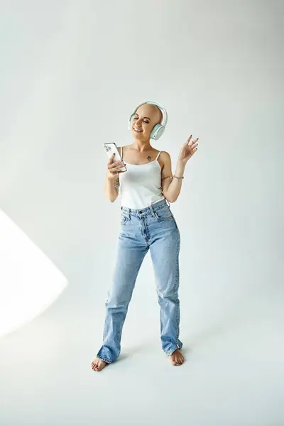 Uma mulher careca alegre dança com seu telefone em um estúdio sereno. — Fotografia de Stock