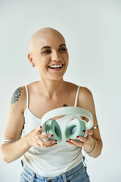 La giovane donna calva irradia felicità mentre afferra le cuffie, circondata dalla luce. — Foto stock