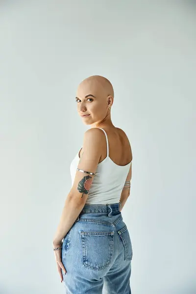 A young bald woman with alopecia stands confidently against a plain backdrop, embracing her beauty. — Stock Photo