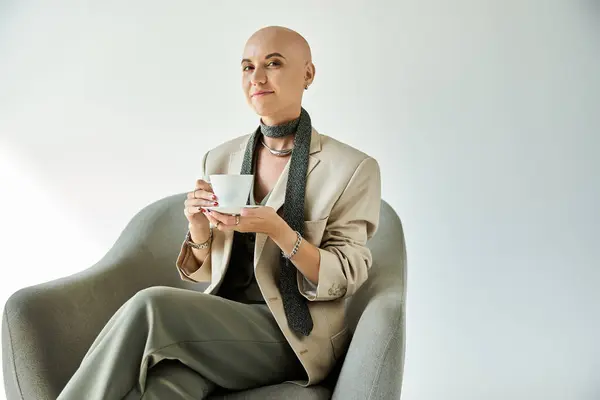 In a serene indoor setting, a confident young woman with a bald head sits elegantly, savoring tea. — Stock Photo