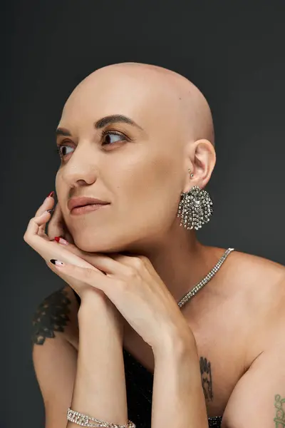 A confident young woman with a bald head admires her reflection, wearing elegant earrings. — Stock Photo