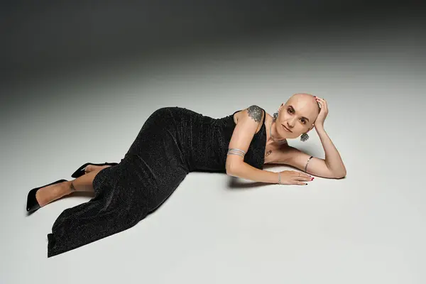 A young bald woman exudes confidence in a stylish black gown while reclining elegantly. — Stock Photo