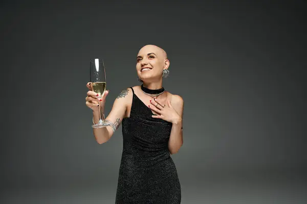 Una joven calva con alopecia levanta alegremente un vaso, encarnando fuerza y elegancia. - foto de stock