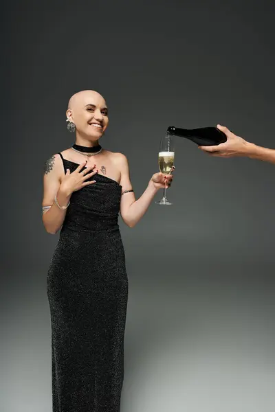 A young bald woman with alopecia smiles brightly while receiving champagne in a stylish setting. — Stock Photo