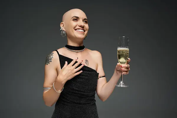 A young woman with alopecia smiles brightly, holding a glass of champagne while dressed elegantly. — Stock Photo