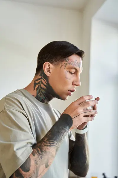 A handsome young man with tattoos takes a moment to enjoy a warm beverage at home. — Stock Photo