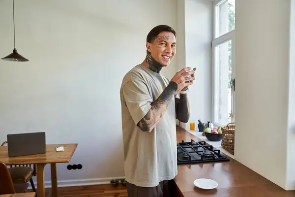 A young man smiles in a bright kitchen, savoring his peaceful time at home with a cup. — Stock Photo