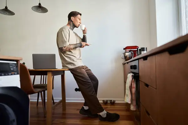 Un bel giovane uomo sta tranquillamente nella sua accogliente casa, sorseggiando una bevanda calda e riflettendo. — Foto stock