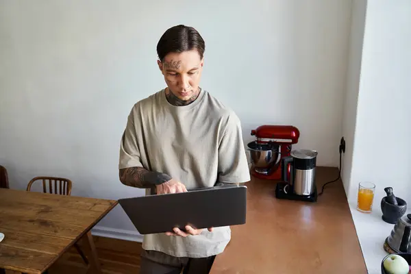 A young man focuses on his laptop while standing in a welcoming kitchen. — Stock Photo