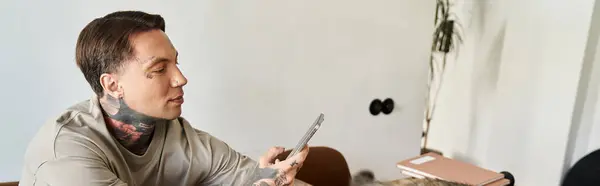 A young man with tattoos enjoys a leisurely moment, engaged in texting at home. — Stock Photo