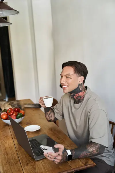 This young man joyfully sips coffee while engaged with his laptop in a warm, inviting space. — Stock Photo