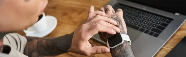 Em um ambiente doméstico quente, um jovem examina seu smartwatch enquanto está sentado em uma mesa. — Fotografia de Stock