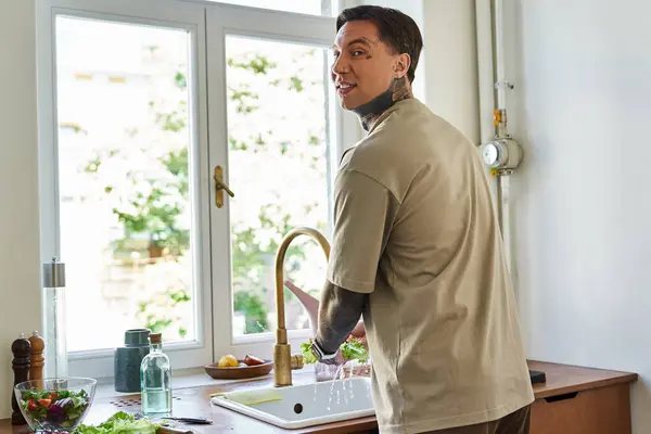 The young man smiles while preparing a fresh meal in his cozy, sunlit kitchen. — Stock Photo