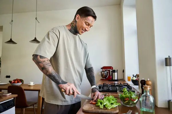 Un bel giovane uomo sorride mentre taglia verdure fresche in una cucina luminosa e invitante. — Foto stock