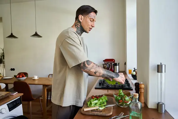 Un giovane bell'uomo si concentra sulla preparazione di un'insalata fresca mentre si gode il suo spazio cucina di casa. — Foto stock