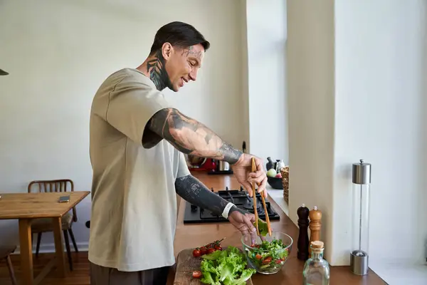 A young handsome man skillfully mixes vegetables in a bowl while cooking at home. — Stock Photo
