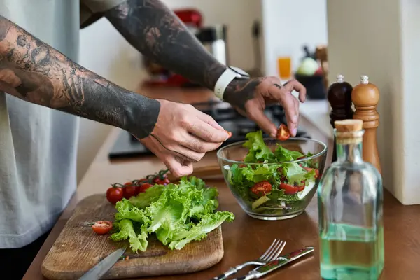 Un jeune homme aime cuisiner, assembler habilement une salade lumineuse et saine dans une cuisine. — Photo de stock