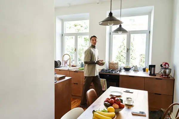 A handsome young man stands in a modern kitchen, surrounded by fresh produce and natural light. — Stock Photo