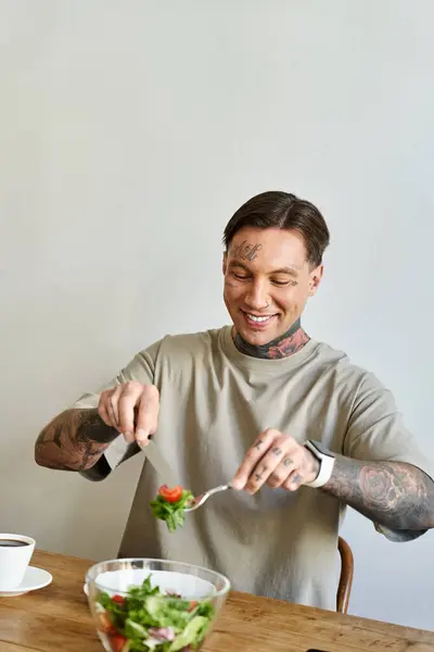 A young man cheerfully prepares a fresh salad at his home while sipping coffee. — Stock Photo