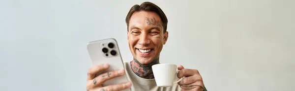 In un accogliente spazio interno, un giovane sorseggia caffè e sorride allo schermo del suo smartphone. — Foto stock