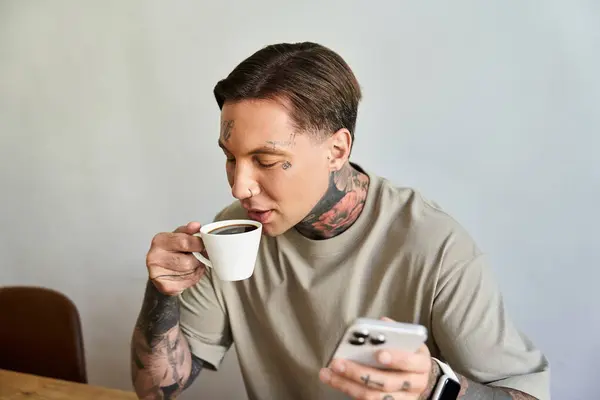Un giovane adora una calda tazza di caffè a casa, curiosando casualmente nel suo smartphone. — Foto stock