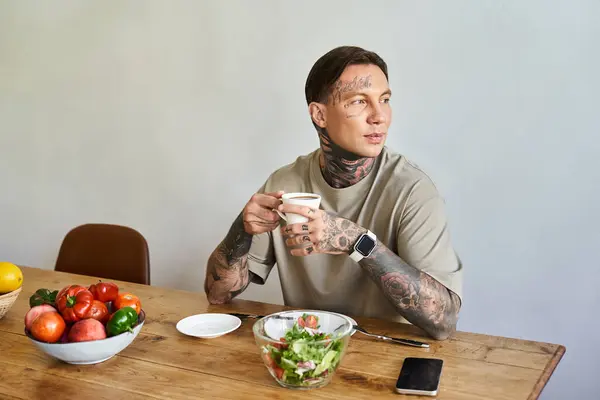 The young man sips his drink while surrounded by fresh vegetables, enjoying a cozy home atmosphere. — Stock Photo