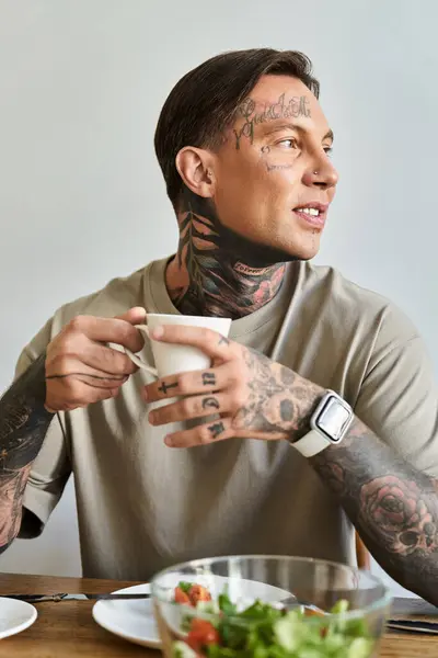 A young man smiles as he savors his coffee at home, surrounded by his breakfast and lifestyle. — Stock Photo
