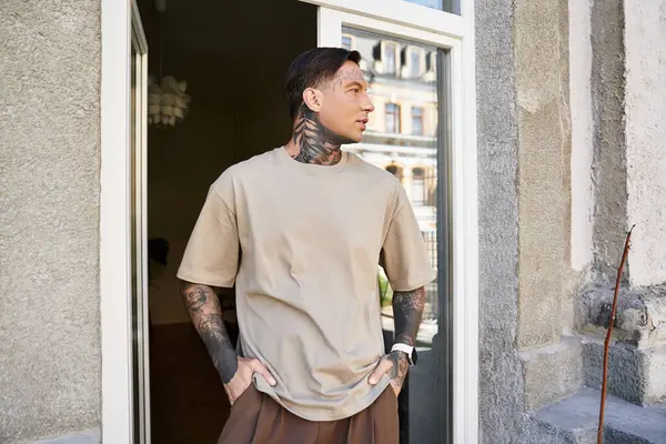 A young man with tattoos leans casually in his doorway, embracing the warmth of the day. — Stock Photo