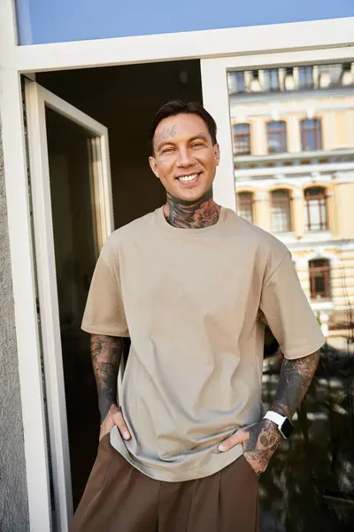 A cheerful young man in casual wear and tattoos relaxes in a brightly lit room. — Stock Photo