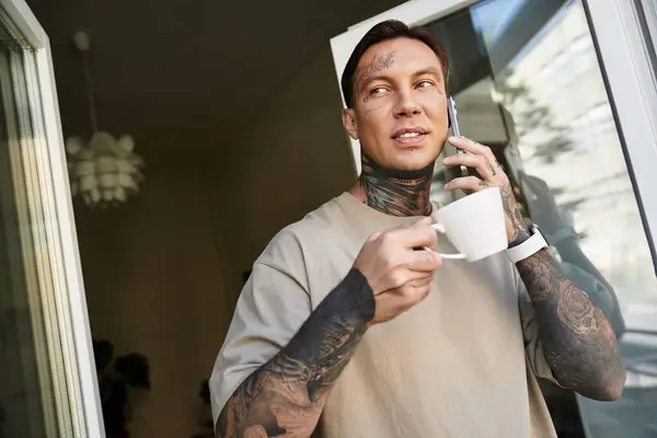 The young man savors his coffee, engaged in a pleasant phone conversation from his home. — Stock Photo