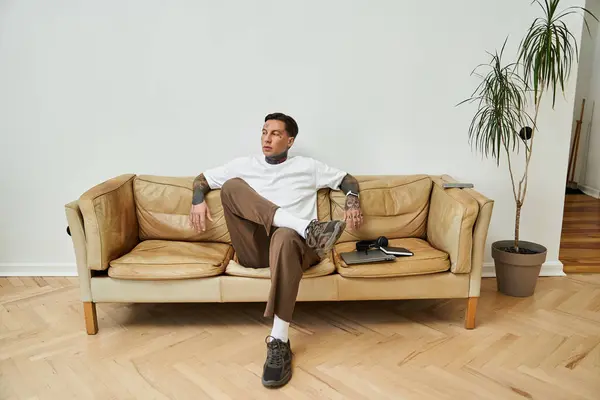 A young handsome man lounges comfortably on a modern sofa, reflecting on his day. — Stock Photo
